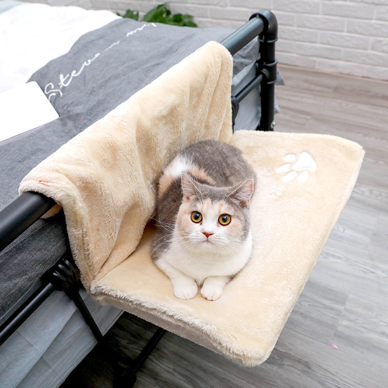 Cat sitting on a plush beige pet bed attached to a bed frame.