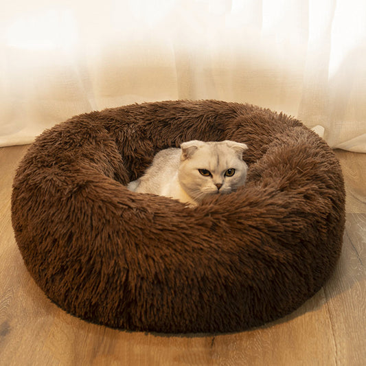 Cat lying in a brown plush donut bed on a wooden floor.