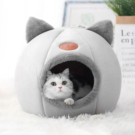 Cat peeking out from a gray cat-shaped pet bed on a white surface.